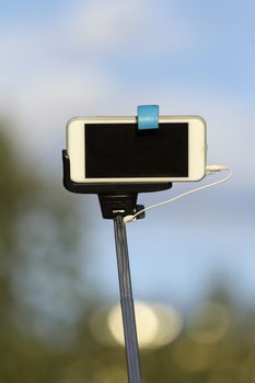 Selfi stick with your Smart-phone against the blue sky and trees