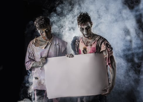 Two Male Zombies Holding Empty White Banner on Dark Background and Smoke