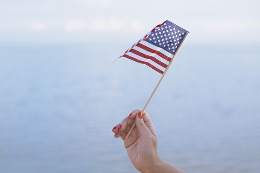 Woman hand holding USA flag in front of the ocean