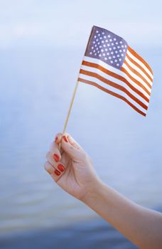 Woman hand holding USA flag in front of the ocean