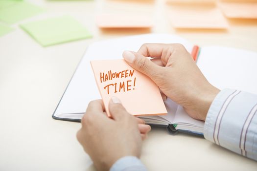 Hands holding sticky note with Halloween Time text