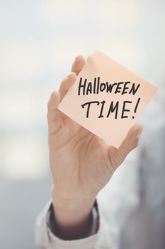 Woman holding sticky note with Halloween time text