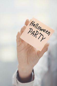 Woman holding sticky note with Halloween party text