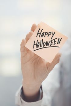 Woman holding sticky note with Happy Halloween text