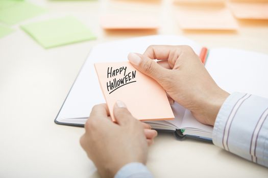 Hands holding sticky note with Happy Halloween text