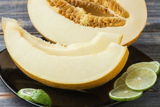 Ripe melon and lime on a black ceramic plate on old boards