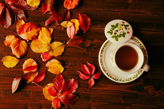 Cup of tea and autumnal foliage over a dark table seen from above
