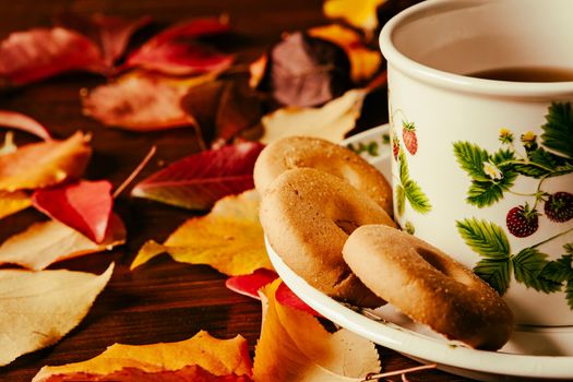 Closeup of cup of tea with biscuits and autumnal foliage over a dark table
