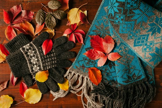 Gloves, scarf and colorful autumnal foliage over a dark table seen from above