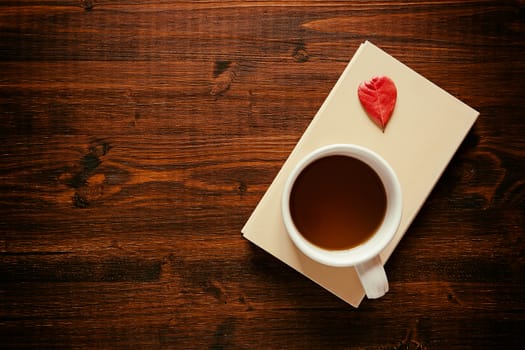 Cup of tea on a book and autumnal leaf over a dark table seen from above