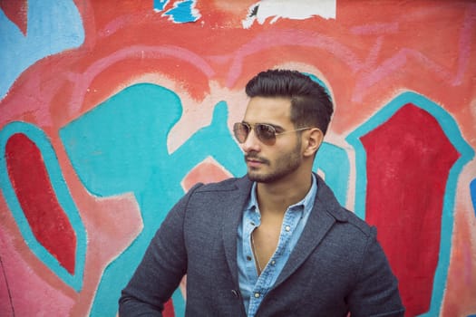 Attractive young man standing against colorful graffiti wall, looking away