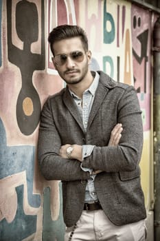 Attractive young man standing against colorful graffiti wall, looking at camera