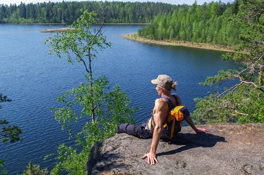 man with backpack sitting on cliff relaxing above the lake Yastrebinoye, Priozersky district in Leningrad region, Russia