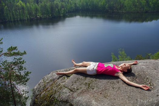 a woman laying on cliff an relaxing above the lake Yastrebinoye, Priozersky district in Leningrad region, Russia