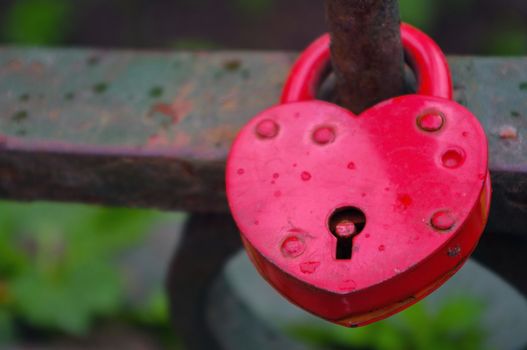Red Padlock in heart style on the fence of a bridge