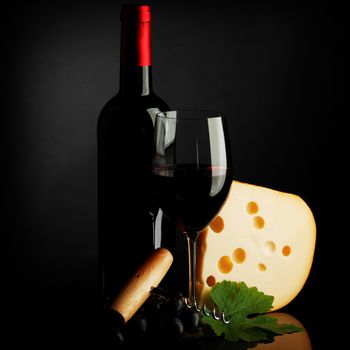 Red wine bottle, glass, cheese and corkscrew on dark background