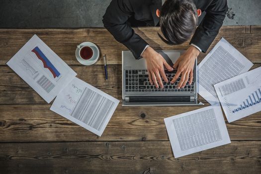 Businessman working on laptop with financial documents, top view