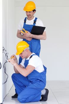 Two builders in helmets working with electricity indoors