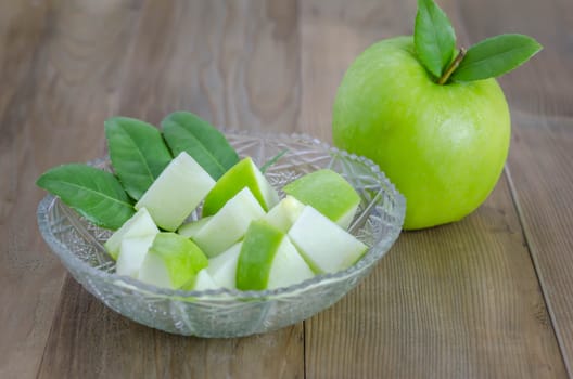 Ripe green apple with leaf and slice on a wooden background