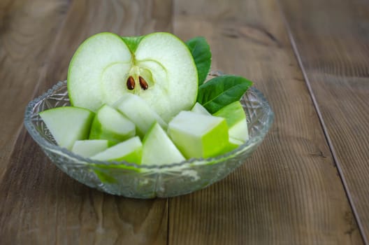 Ripe green apple with leaf and slice on a wooden background