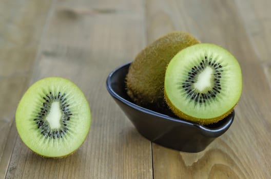 kiwi fruit and half with black bowl on wooden background