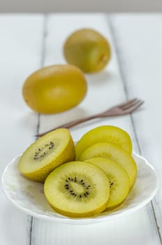 golden kiwi fruit and sliced on dish over white wooden background
