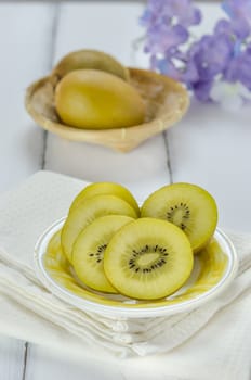 golden kiwi fruit and sliced on dish over white wooden background