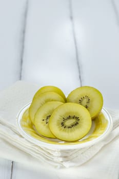 golden kiwi fruit and sliced on dish over white wooden background