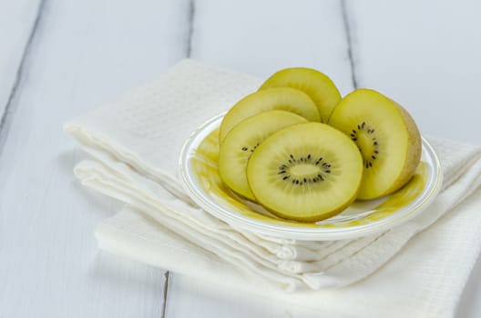 golden kiwi fruit and sliced on dish over white wooden background