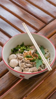 Asian white noodles with pork and vegetables in bowl over wooden background