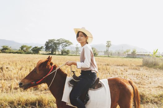 Beautiful young woman is smiling riding a horse on the field with relax time . Sideways to the camera. Freedom, joy, movement