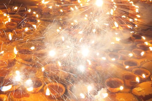 An abstract Diwali background of fireworks and sparklers on traditional lamps.