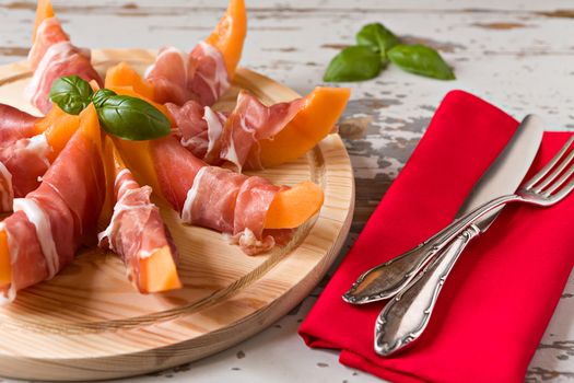 Cutting board with prosciutto and melon over a wooden background