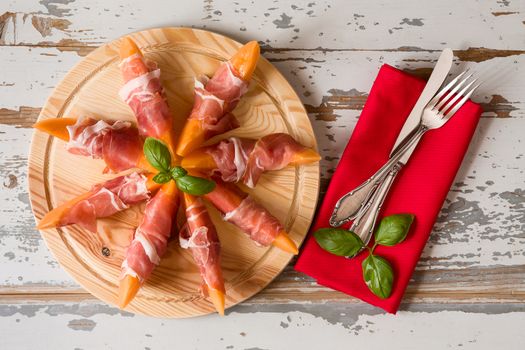 Italian appetizer with prosciutto and melon over a wooden background