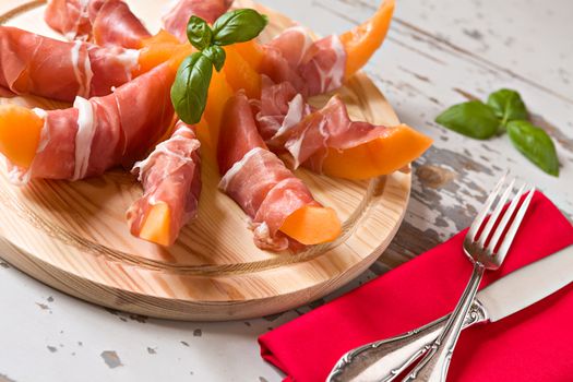 Italian cutting board with prosciutto and melon over a wooden background