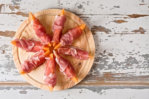 Italian food with prosciutto and melon over a wooden background