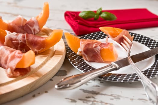 Italian prosciutto with melon on a plate over a wooden background