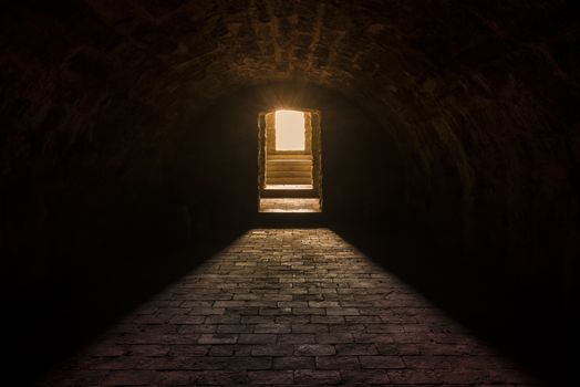 Medieval European basement interior, with round ceiling and stone floor, with strong sun lights at the entrance