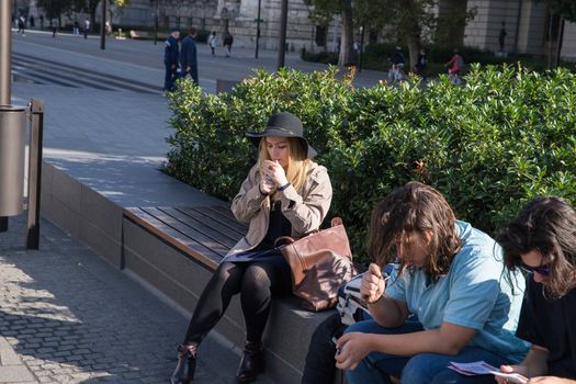 Young fat woman in a hat smokes, sitting on a bench. Smoking molodesh. Youth on the bench. Girl with a cigarette. Summer day.