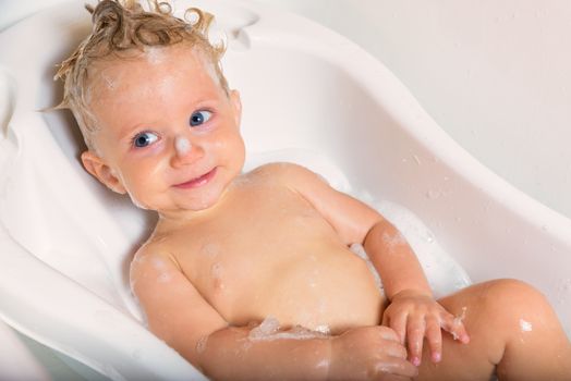 Little pretty wet baby boy in bath room sitting and smiling on white background, horizontal picture.