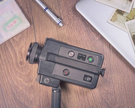 Vintage image with old black Video camera 8mm,old photo,laptop,pen and passport on wood table.