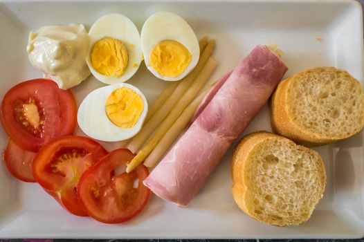 half boiled eggs, sliced tomatoes, bread, ham in a plate. French food