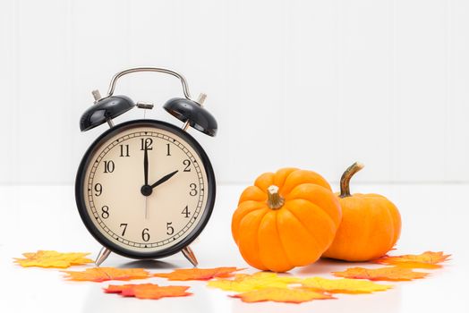 Alarm clock with colorful fall leaves and pumpkins to represent the concept of daylight savings time.