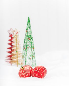 Two red glass Christmas decorations with colorful trees in the background.