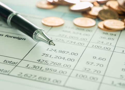 pen and golden coins on summary report. selective focus.