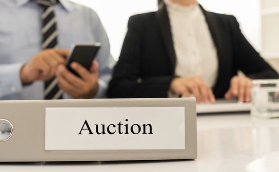 closeup auction file with  two business person bidding via electronic industries in background.