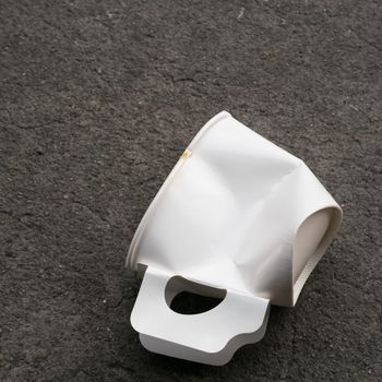 The close up of disposable paper cup garbage (used coffee cup) on cement ground.