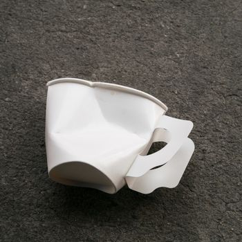 The close up of disposable paper cup garbage (used coffee cup) on cement ground.