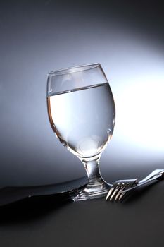 One glass of water near fork and knife on dark background