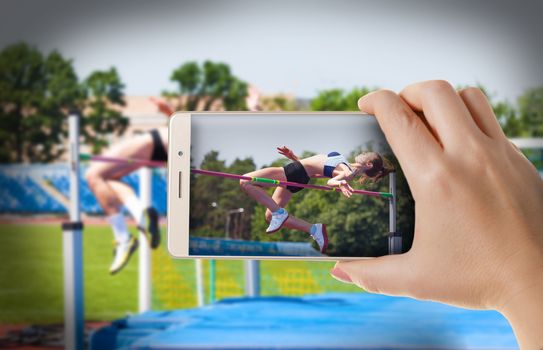  Hands with the phone close-up.Woman photographs sporting competitions athletes on smartphone